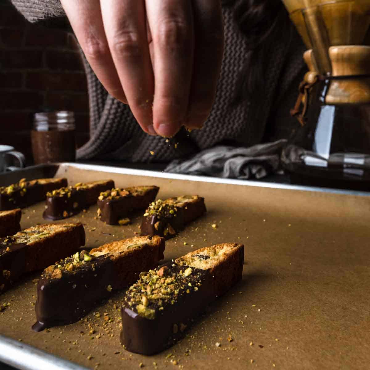 Sprinkling chopped pistachios on chocolate dipped biscotti
