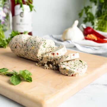 A log of sliced chimichurri butter on a cutting board.