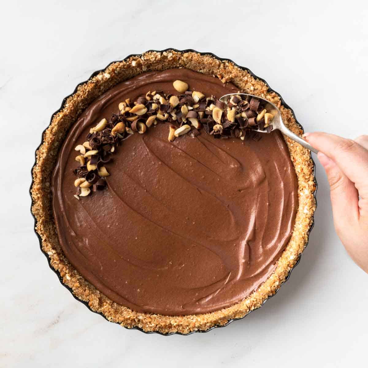 Spooning the roasted peanuts and chocolate curls over the top of the pie