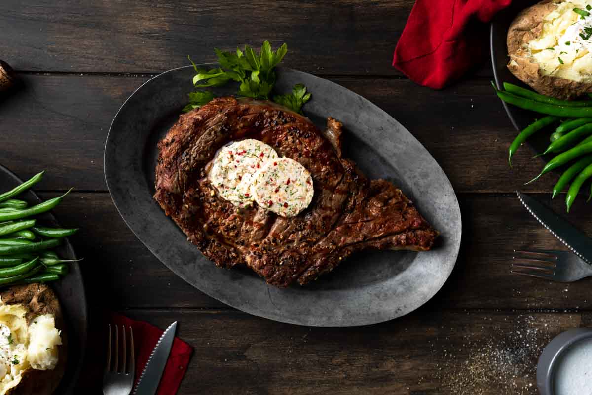 A grilled ribeye on a platter with compound butter