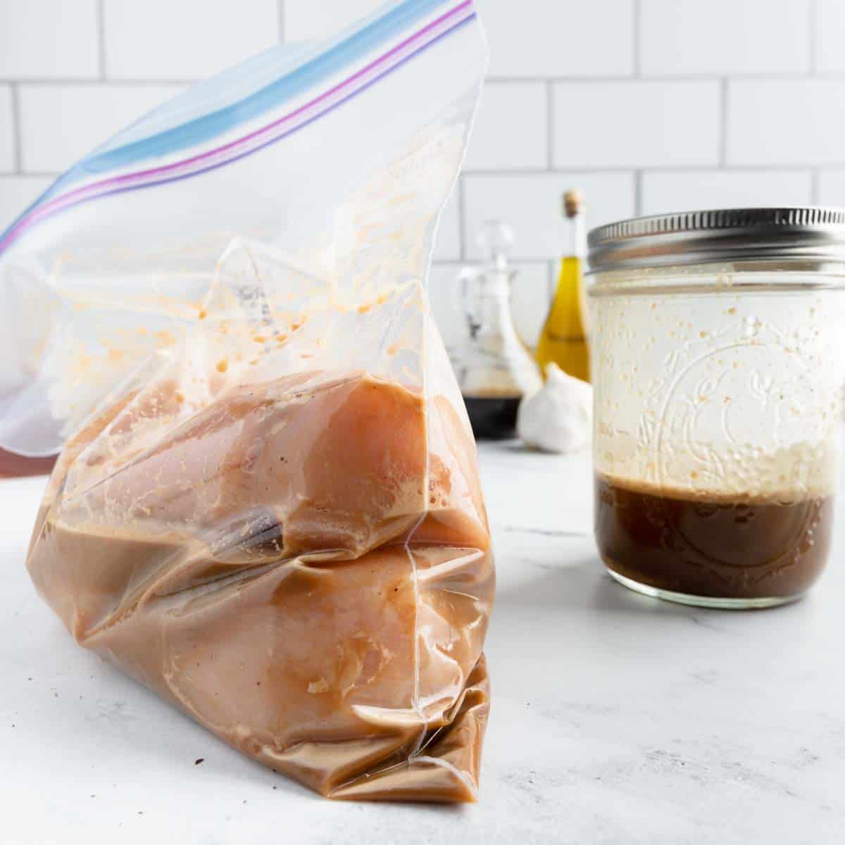 A bag of marinating chicken breasts and a jar with leftover marinade