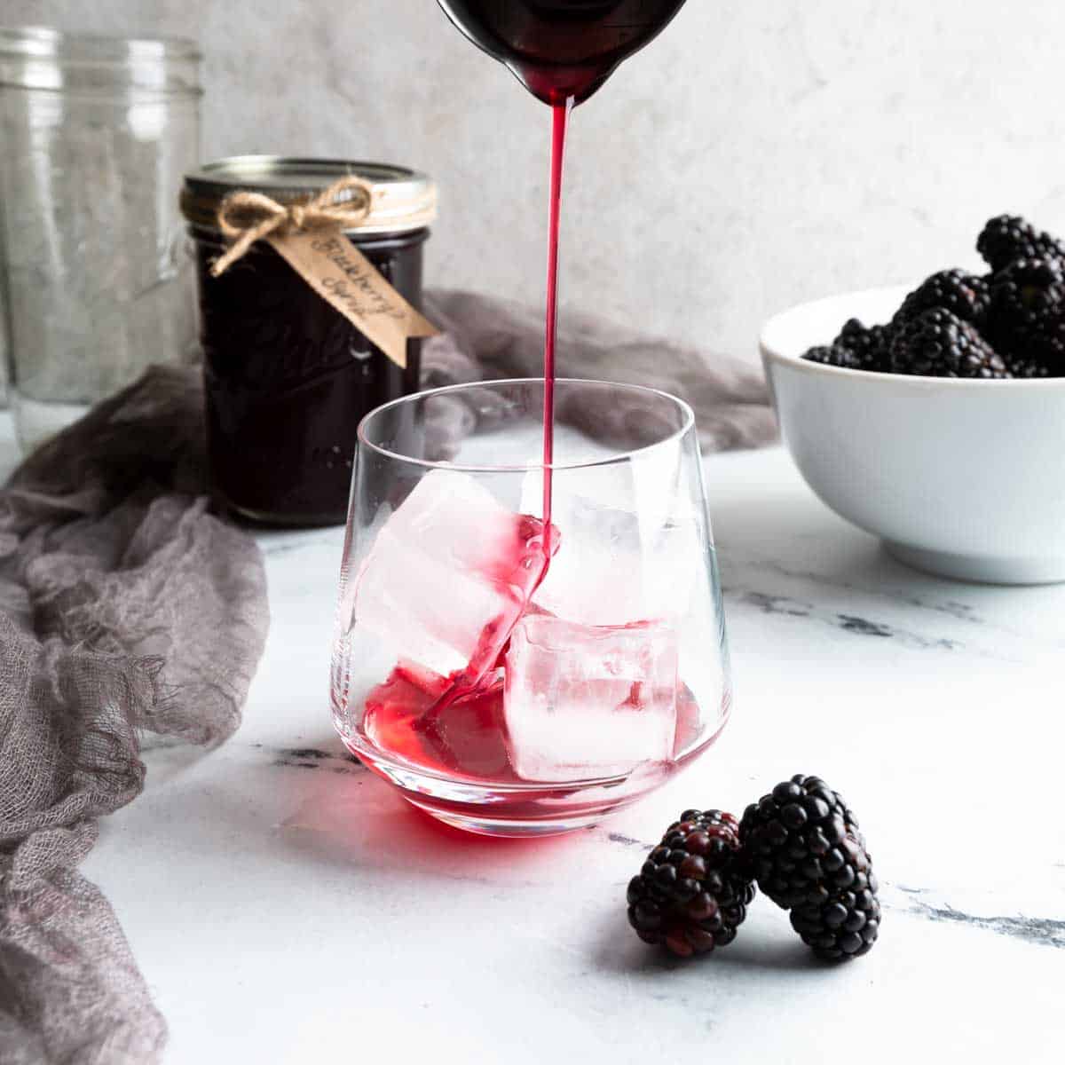 Pouring blackberry syrup in a glass with ice.