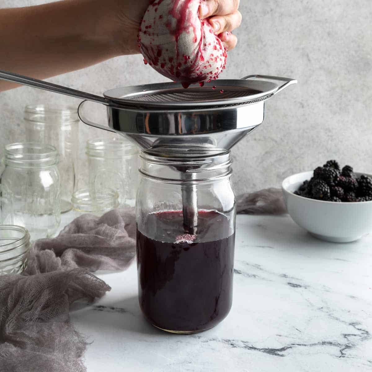 squeezing the berries in cheesecloth over a mason jar