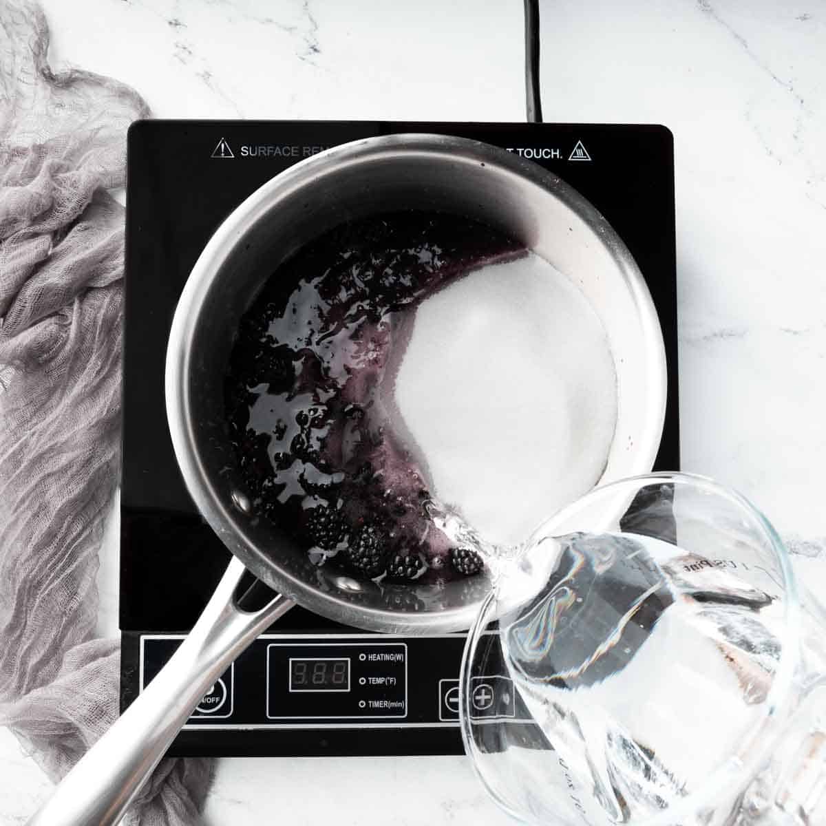 Pouring granulated sugar and water over the blackberries on the pot