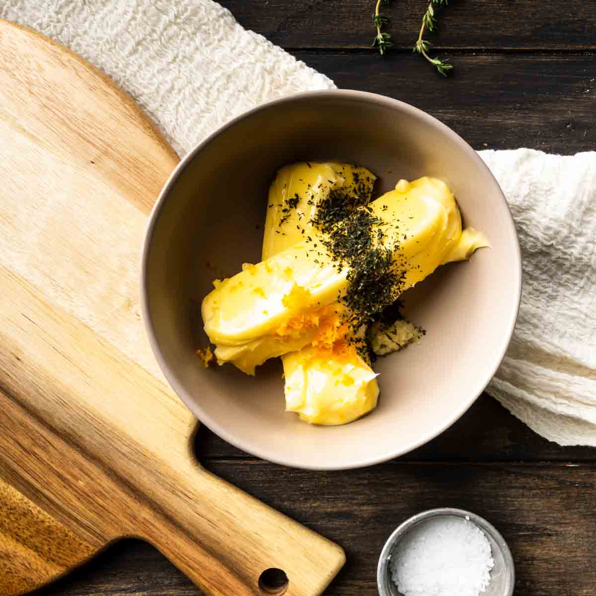 A bowl with two stick of softened butter, thyme, orange zest and grated garlic