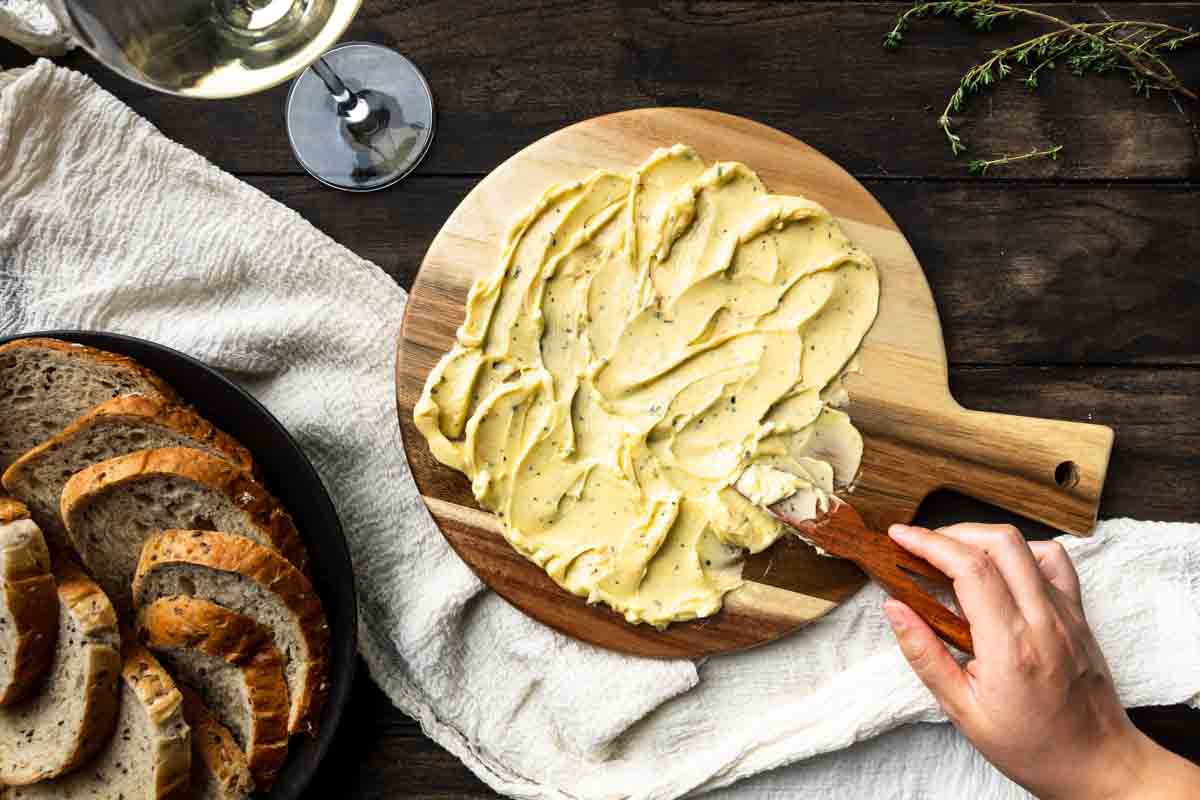 Using a wooden spreader to spread herb butter over a circular board