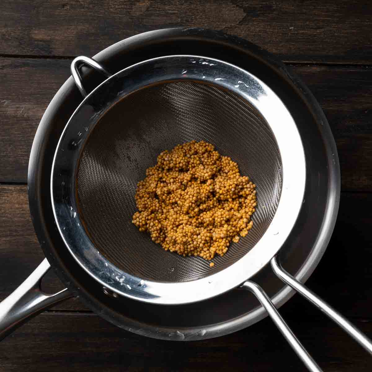 Yellow mustard seeds draining in a fine mesh strainer