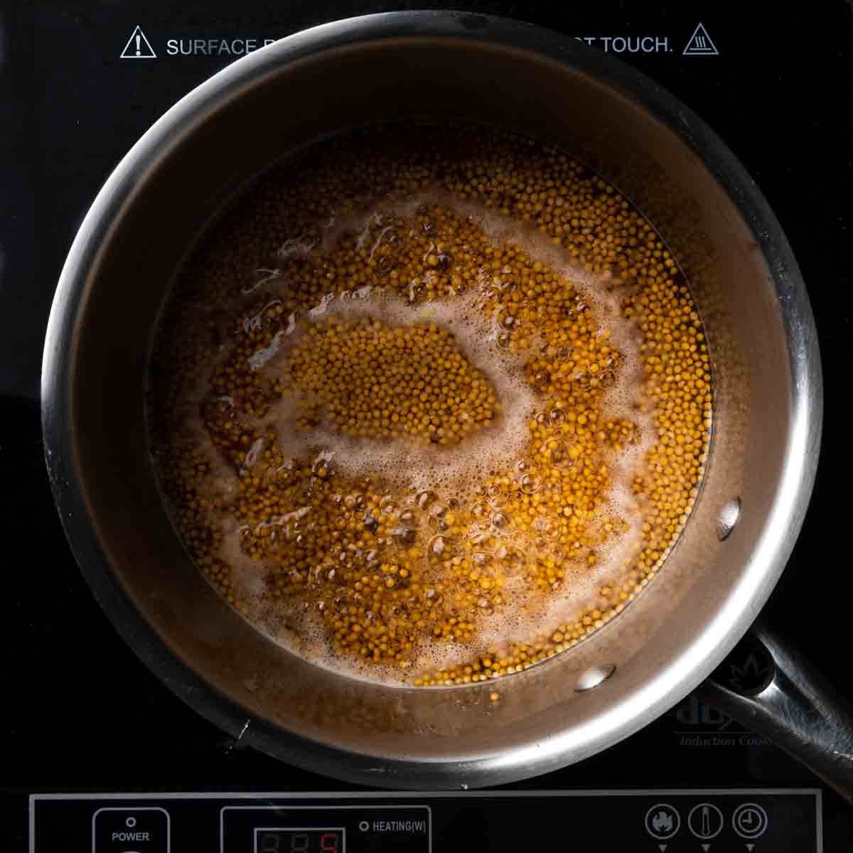 Yellow mustard seeds, vinegar and water simmering in a small pot
