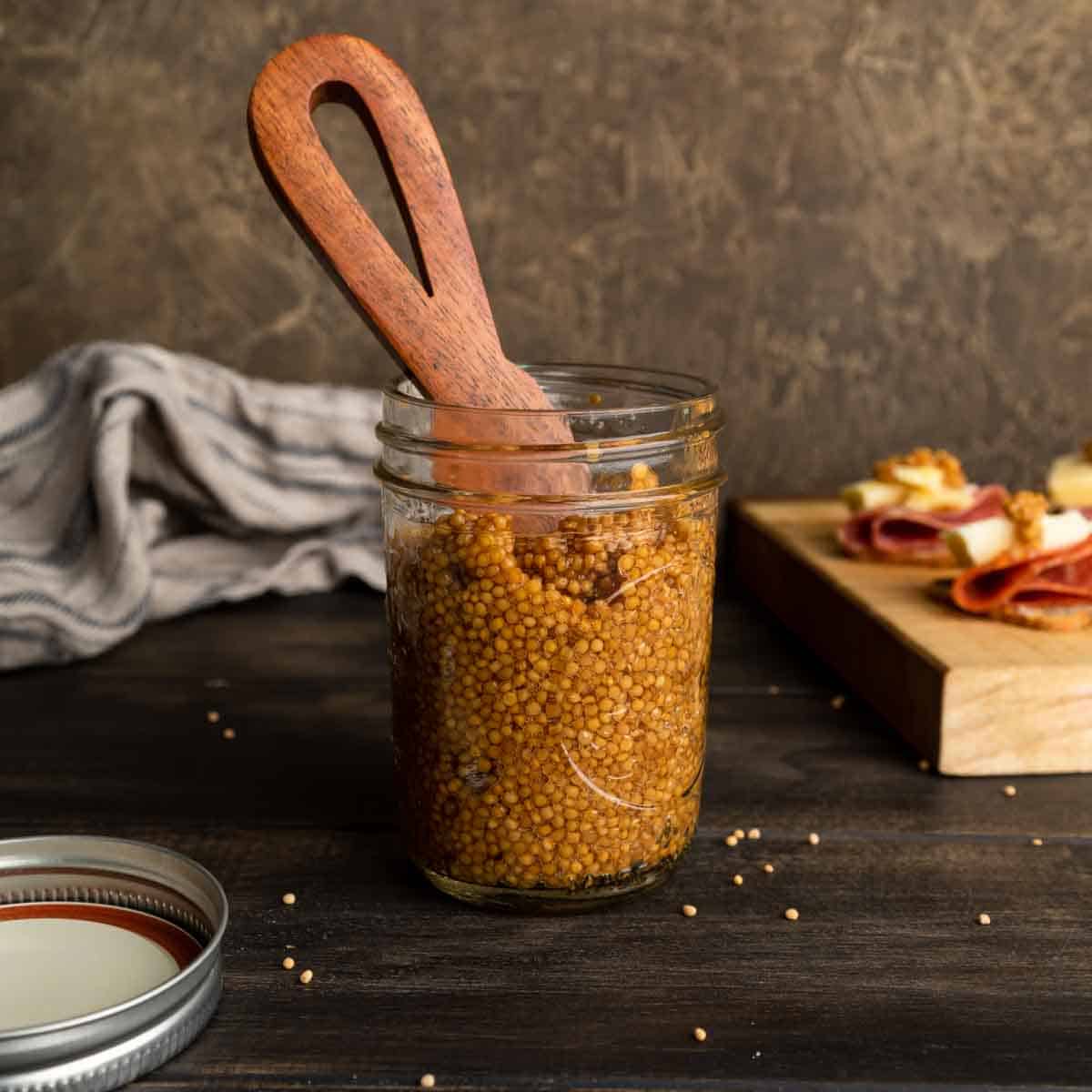 A jar of pickled mustard seeds with a wooden spreader
