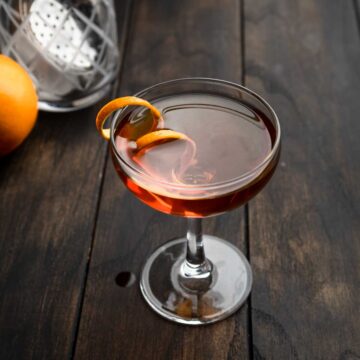 An amontillado sherry manhattan cocktail in a coupe glass garnished with a curly orange peel