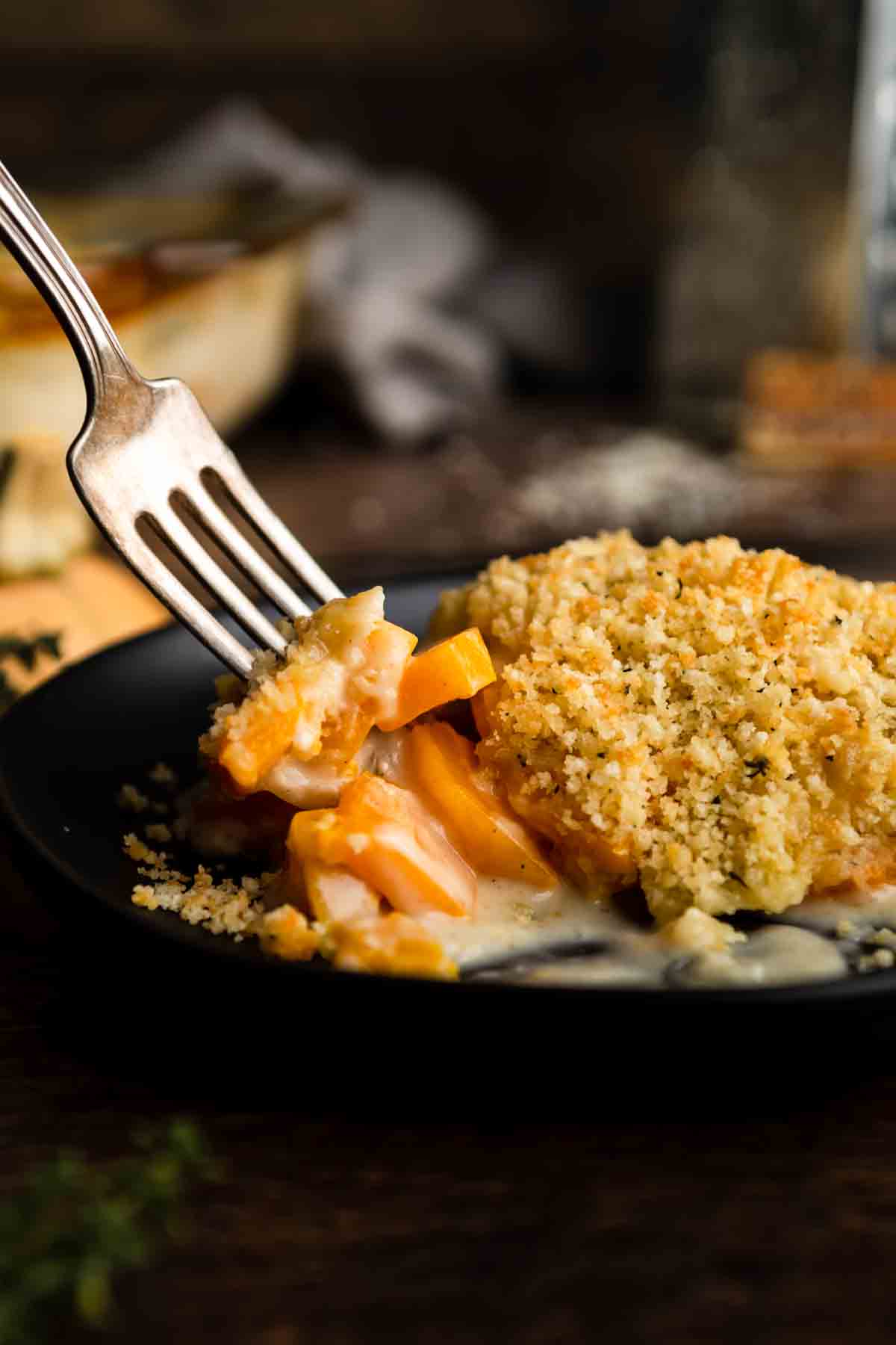A fork digging into a cheesy butternut squash au gratin covered in toasted breadcrumbs