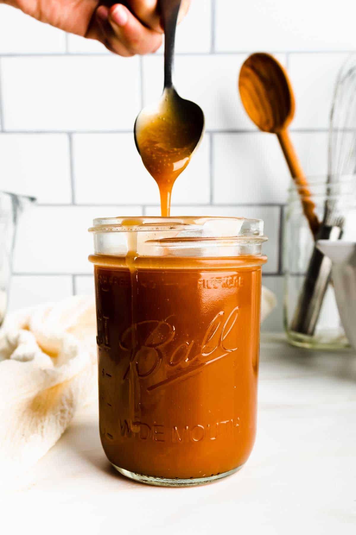 Drizzling caramel sauce from a spoon into a mason jar
