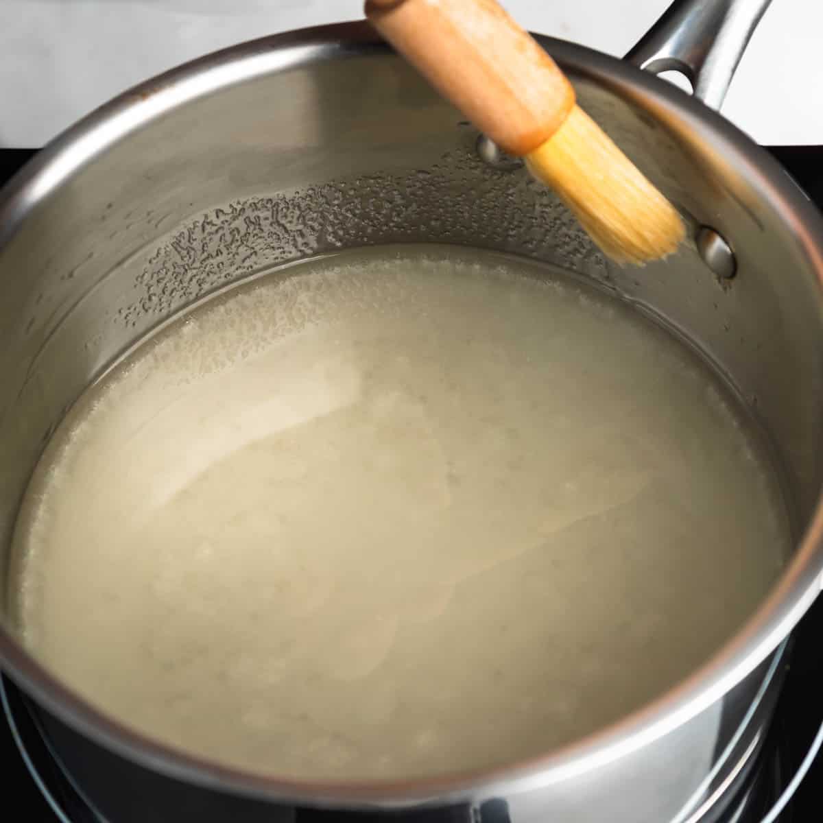 Using a wet pastry brush to wipe sugar from the side of the pot