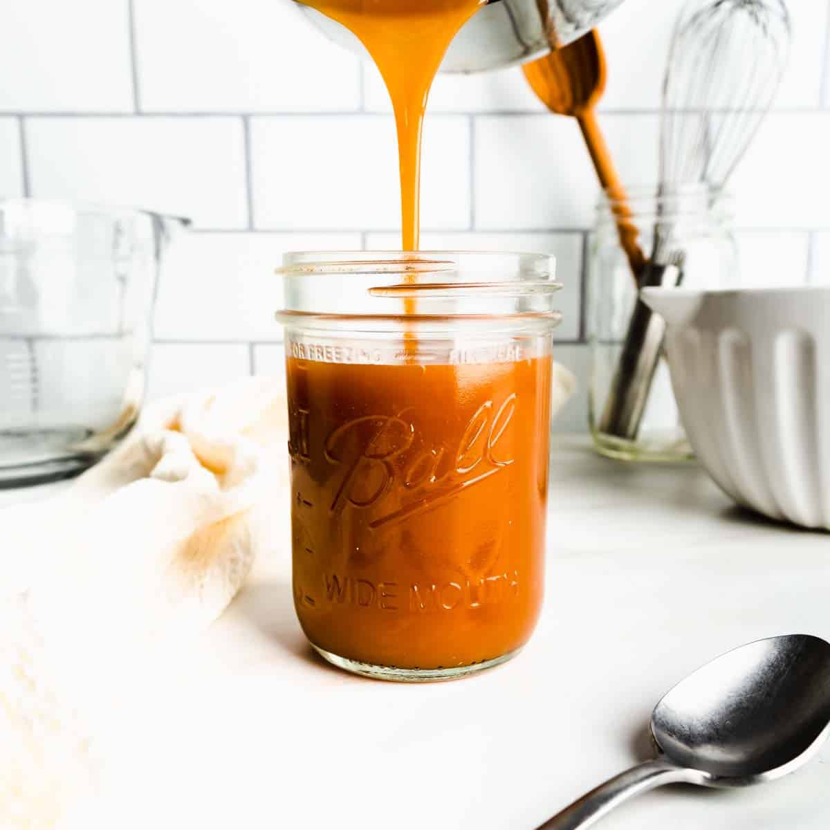 Pouring hot caramel sauce from the pot into a glass mason jar.