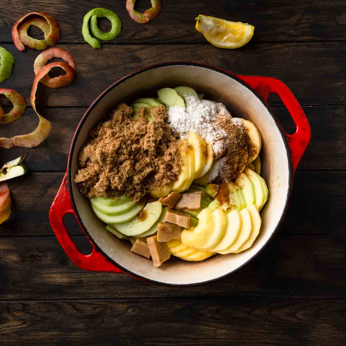 A red dutch oven filled with sliced apples and other ingredients for apple pie filling