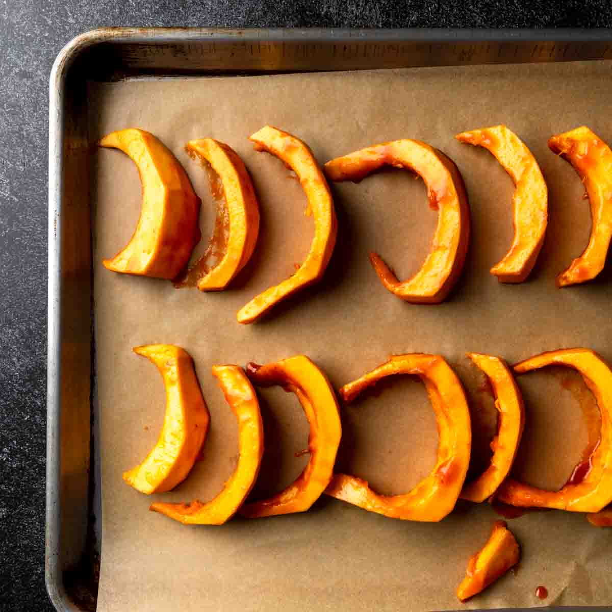 Glazed pumpkin wedges lined up on a baking sheet.