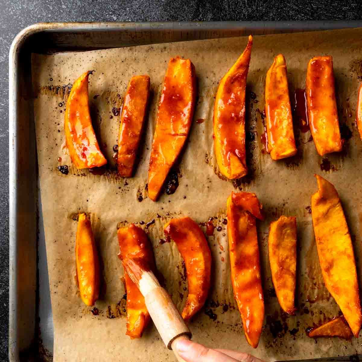 Glazing the roasted pumpkin wedges with more maple gochujang glaze.