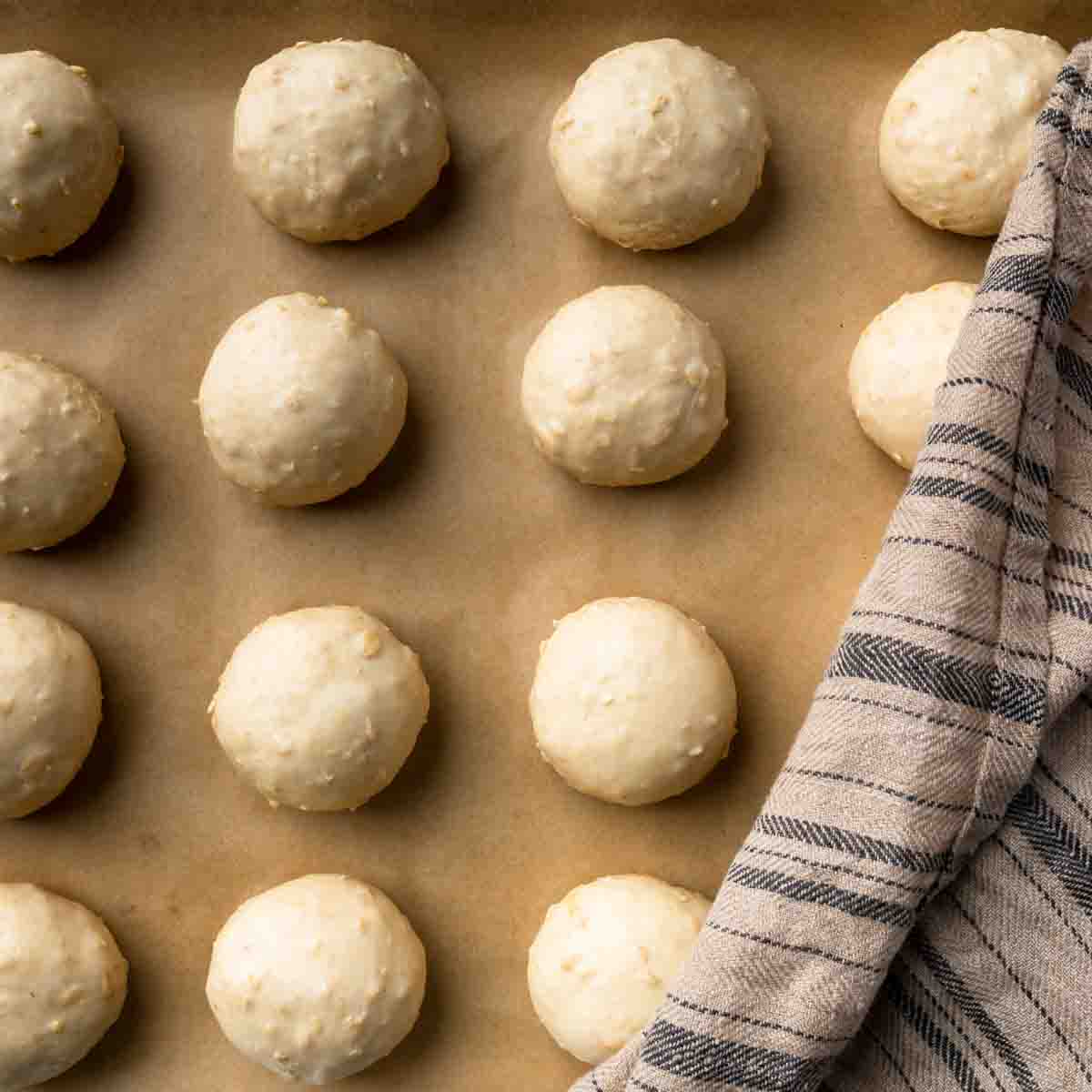 Balls of oatmeal roll dough lined up on a baking sheet