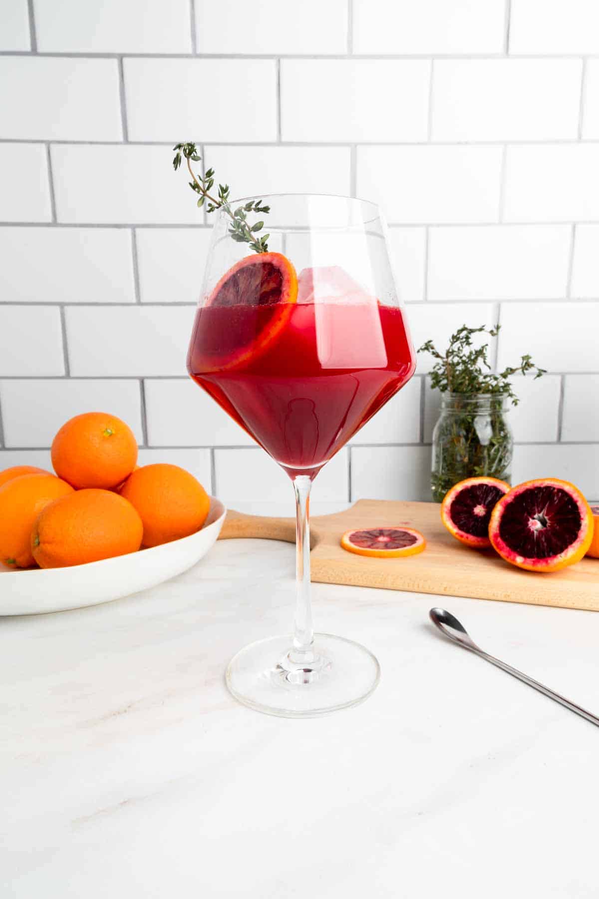 A wine glass filled with a sparkling blood orange mocktail made with thyme syrup.