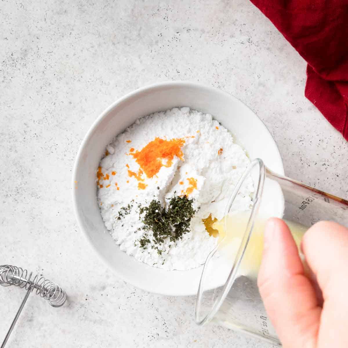 A small mixing bowl with powdered sugar, orange zest and juice and minced thyme leaves. 