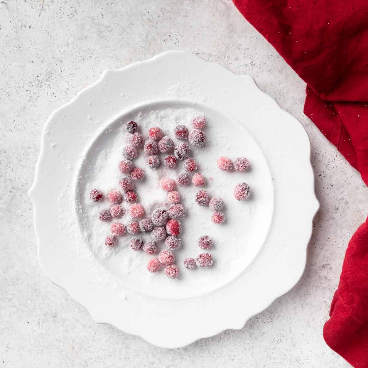 Sugared cranberries on a white plate with granulated sugar. 