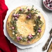 An overhead shot of a cranberry Christmas cake topped with a sugared thyme and cranberry wreath decoration.