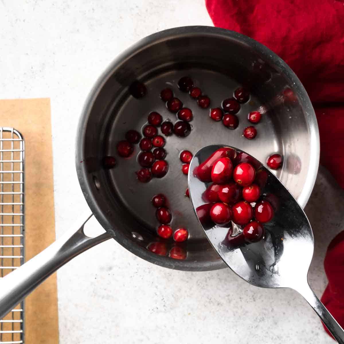 A spoonful of cranberries over a pot of simple syrup.