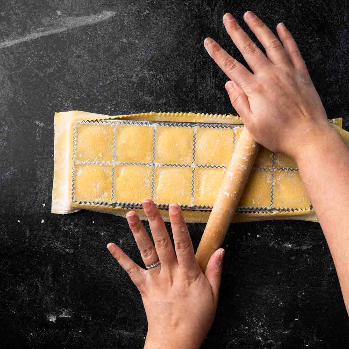 Using a mini rolling pin to seal and cut ravioli in a ravioli tray maker.