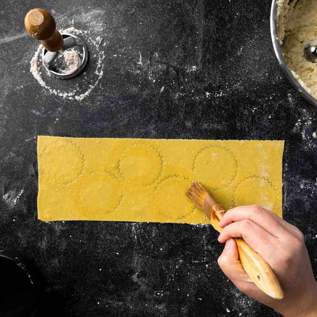 Using a damp pastry brush to moisten the edges of the ravioli indentations. 