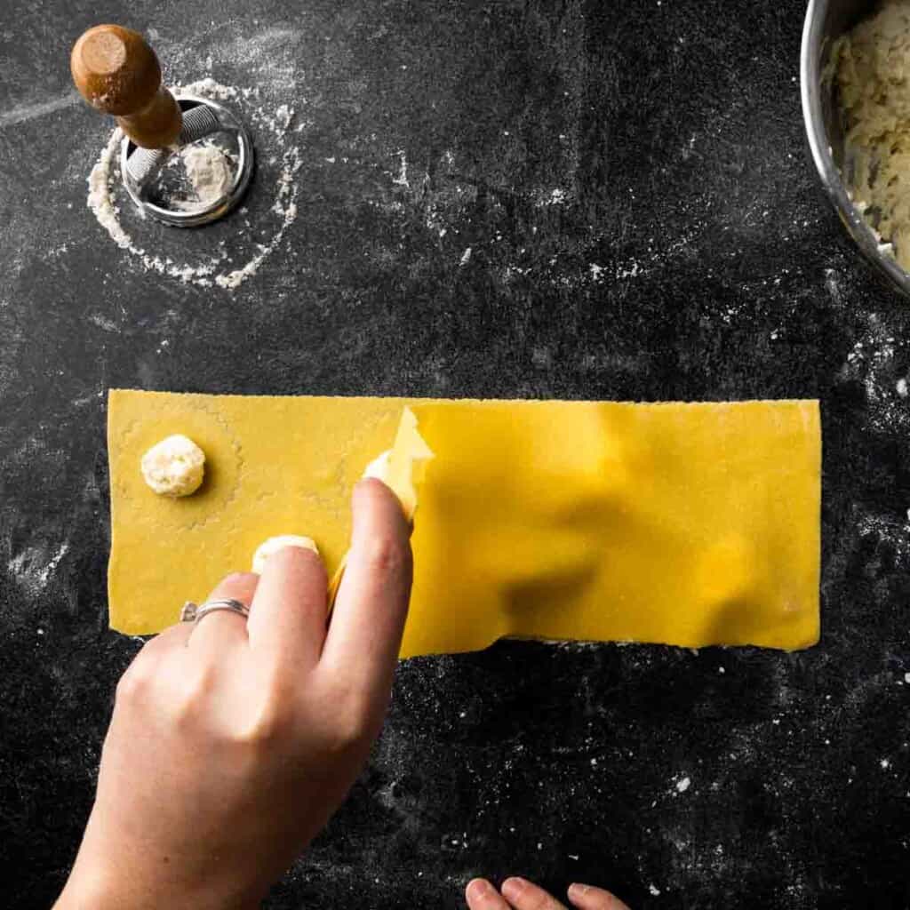 Laying a second sheet of pasta dough over the lumps of ravioli filling.
