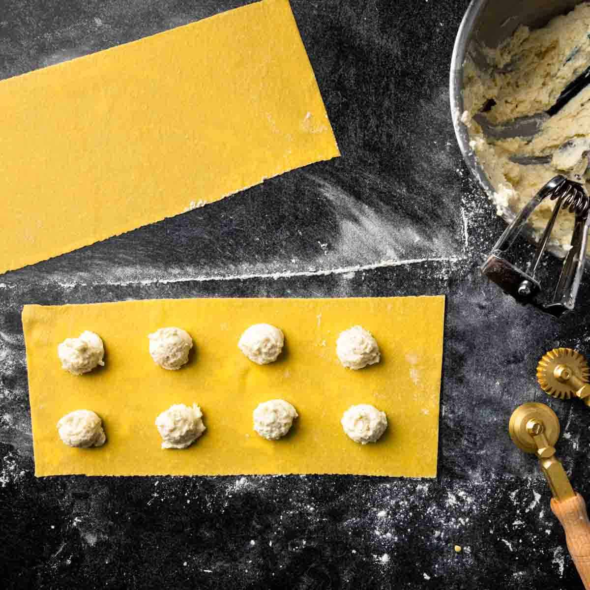 Scoops of pasta filling on a sheet of fresh pasta dough.