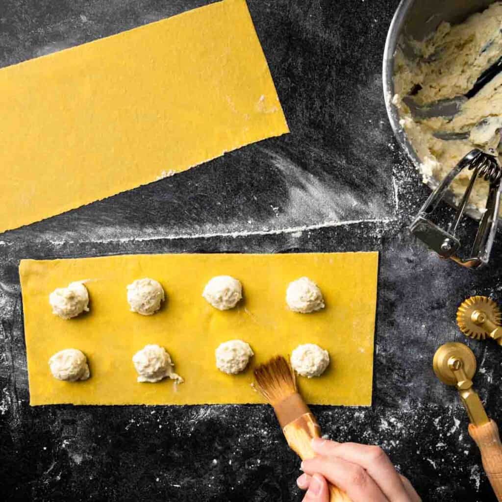 Lightly wetting the pasta dough around the edges of ravioli filling.