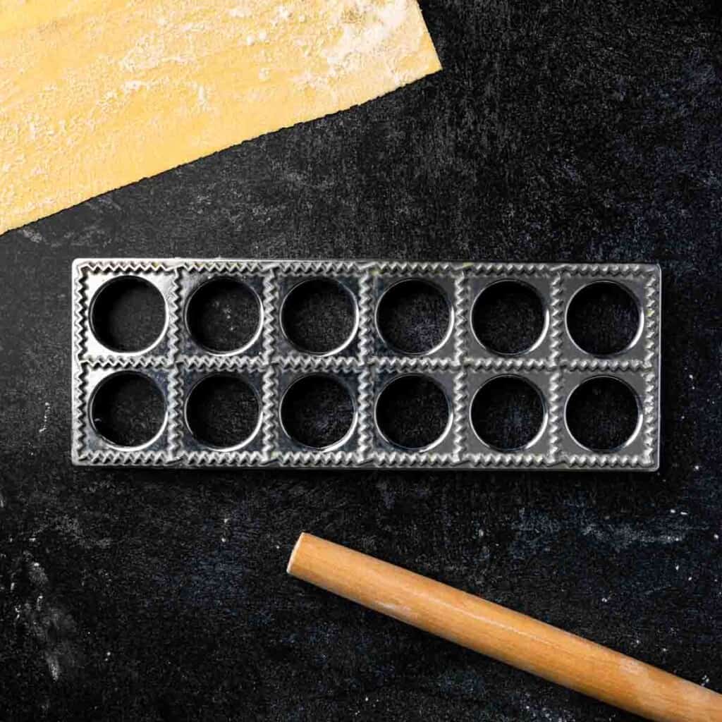 A metal ravioli maker frame and a mini rolling pin.