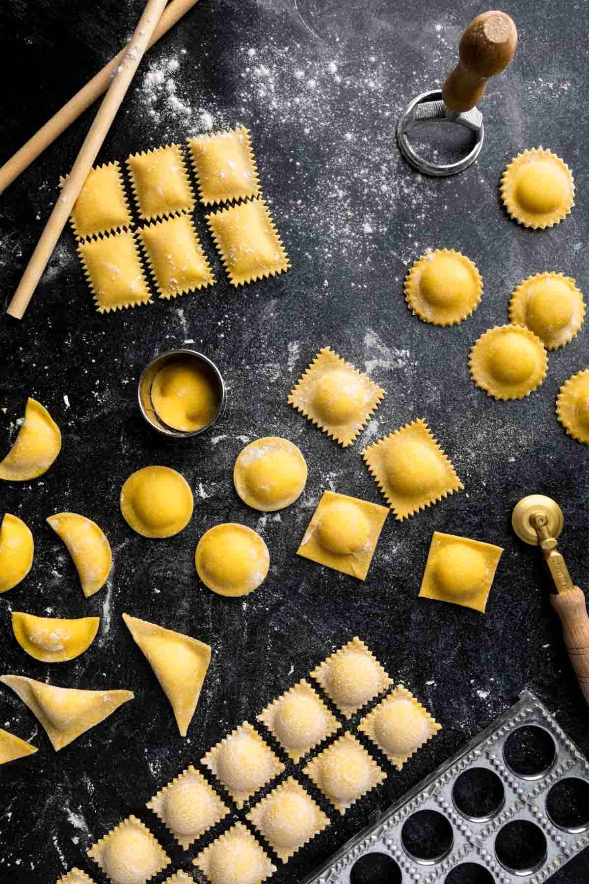 Several shapes of homemade ravioli and fresh pasta making tools.
