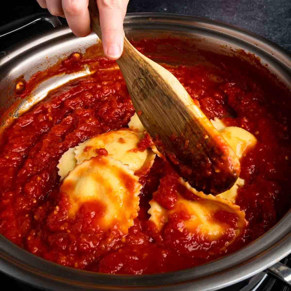 Stirring homemade Italian cheese ravioli in a pan of tomato sauce.