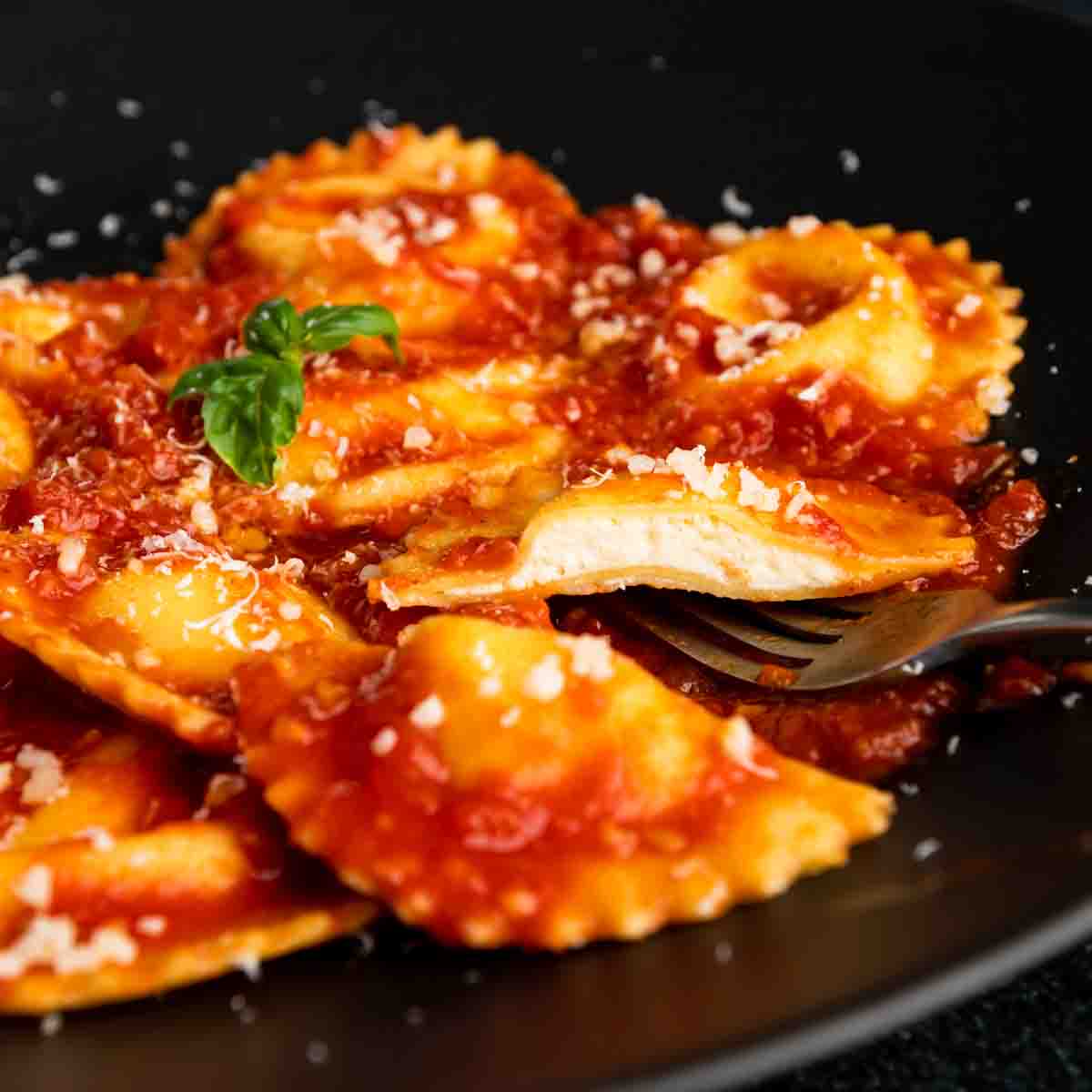 A plate of four cheese ravioli in san Marzano tomato sauce with one cut in half. 