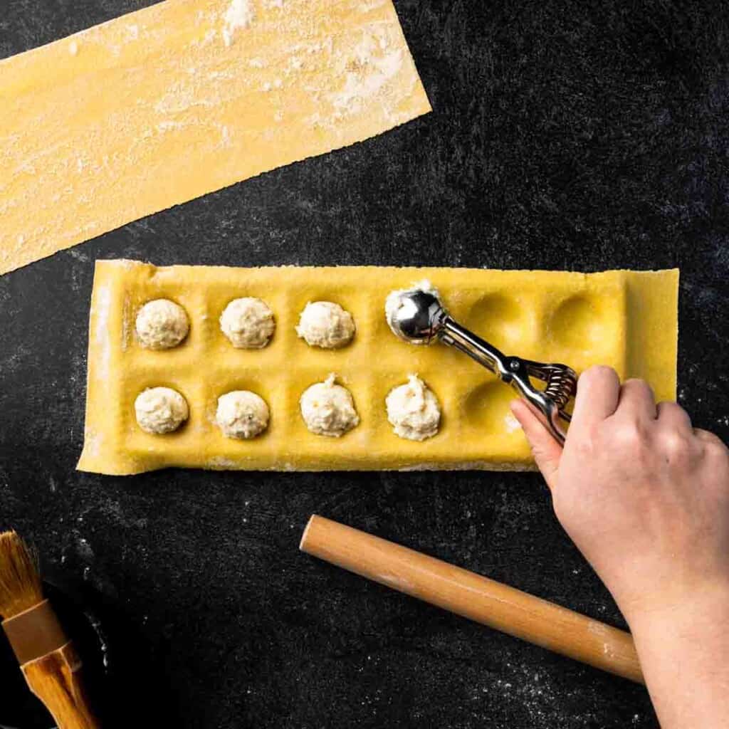 Scooping ravioli filling onto pasta in a ravioli mold.