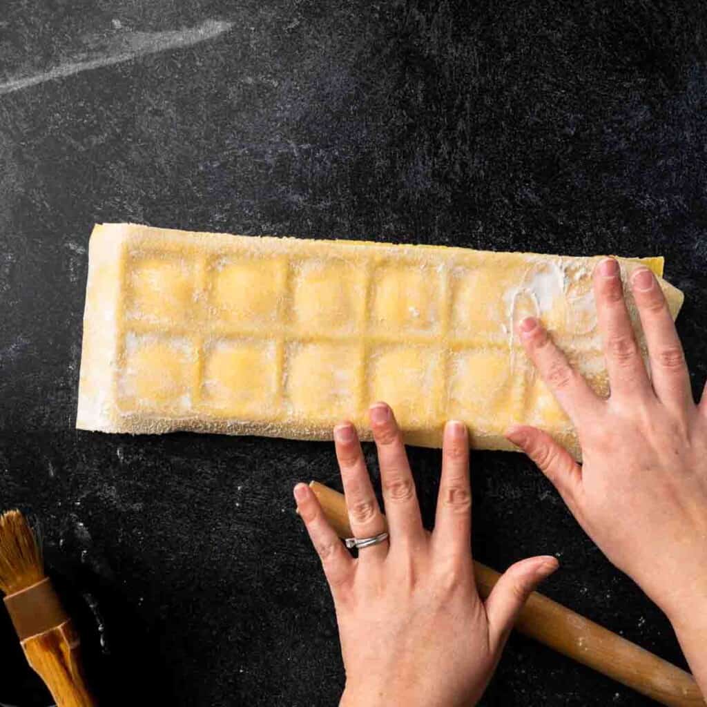 Fingertips sealing the edges of fresh pasta in a ravioli maker.