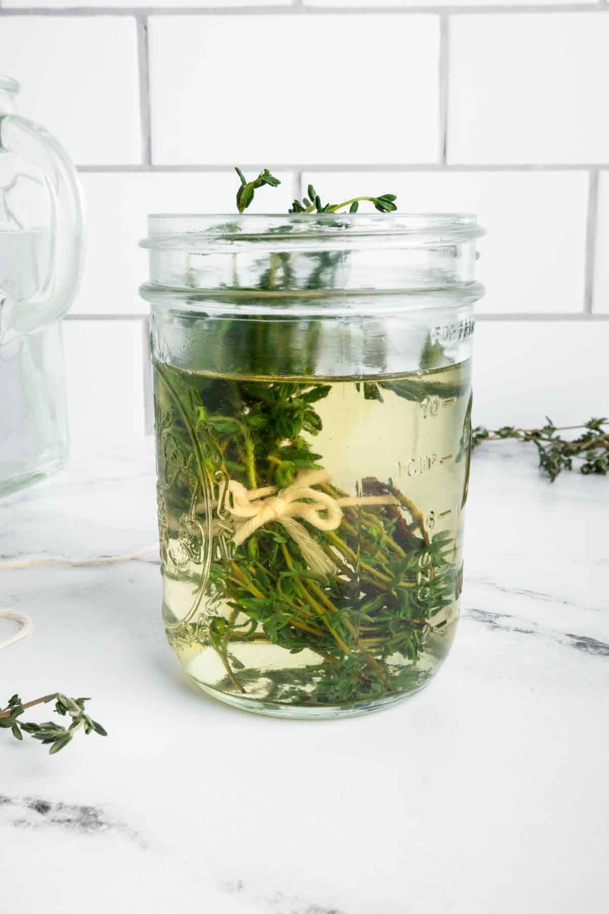 Thyme simple syrup in a mason jar with a bundle of fresh thyme.