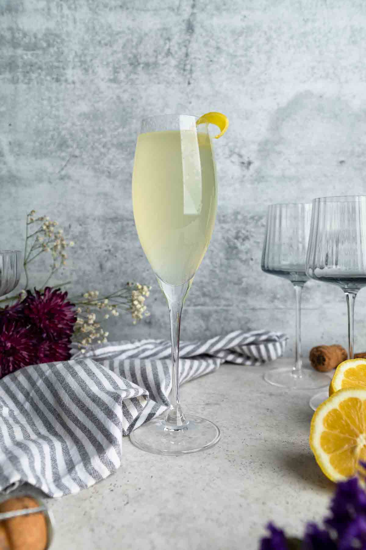 A French 76 cocktail in a Champagne flute with a lemon and flowers.