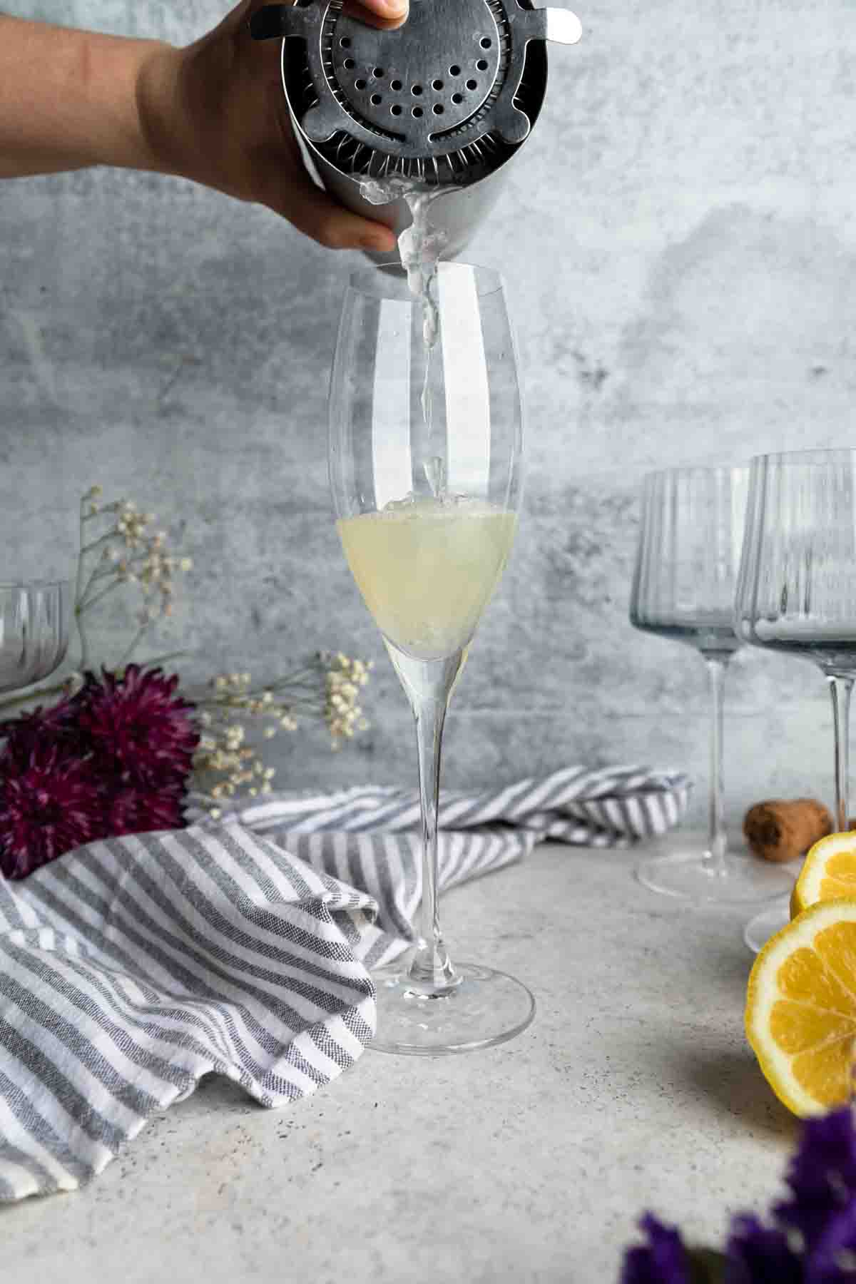 Pouring shaken lemon juice, vodka and simple syrup into a Champagne flute.