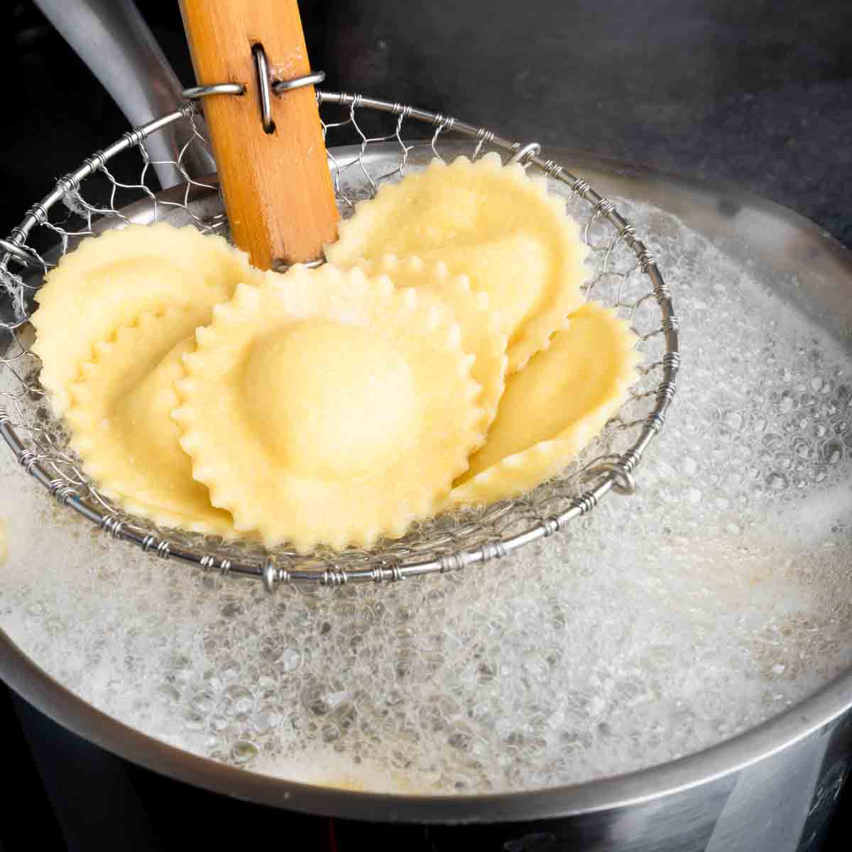 A spider tool gently lifting homemade ravioli out of a pot of boiling water. 