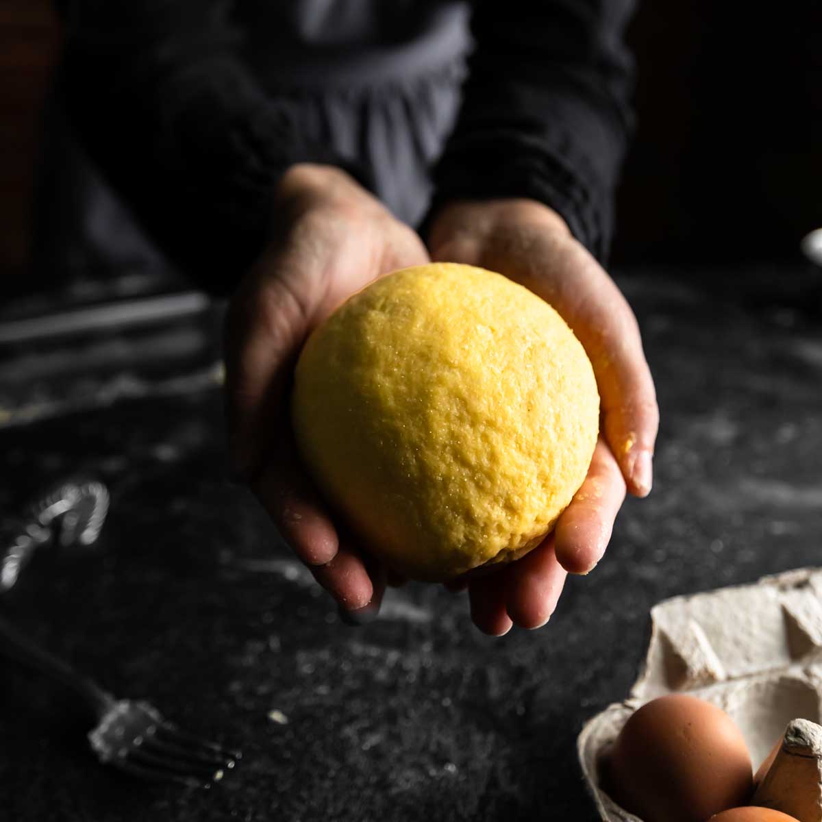 Two hands holding out a ball of fresh semolina pasta dough.