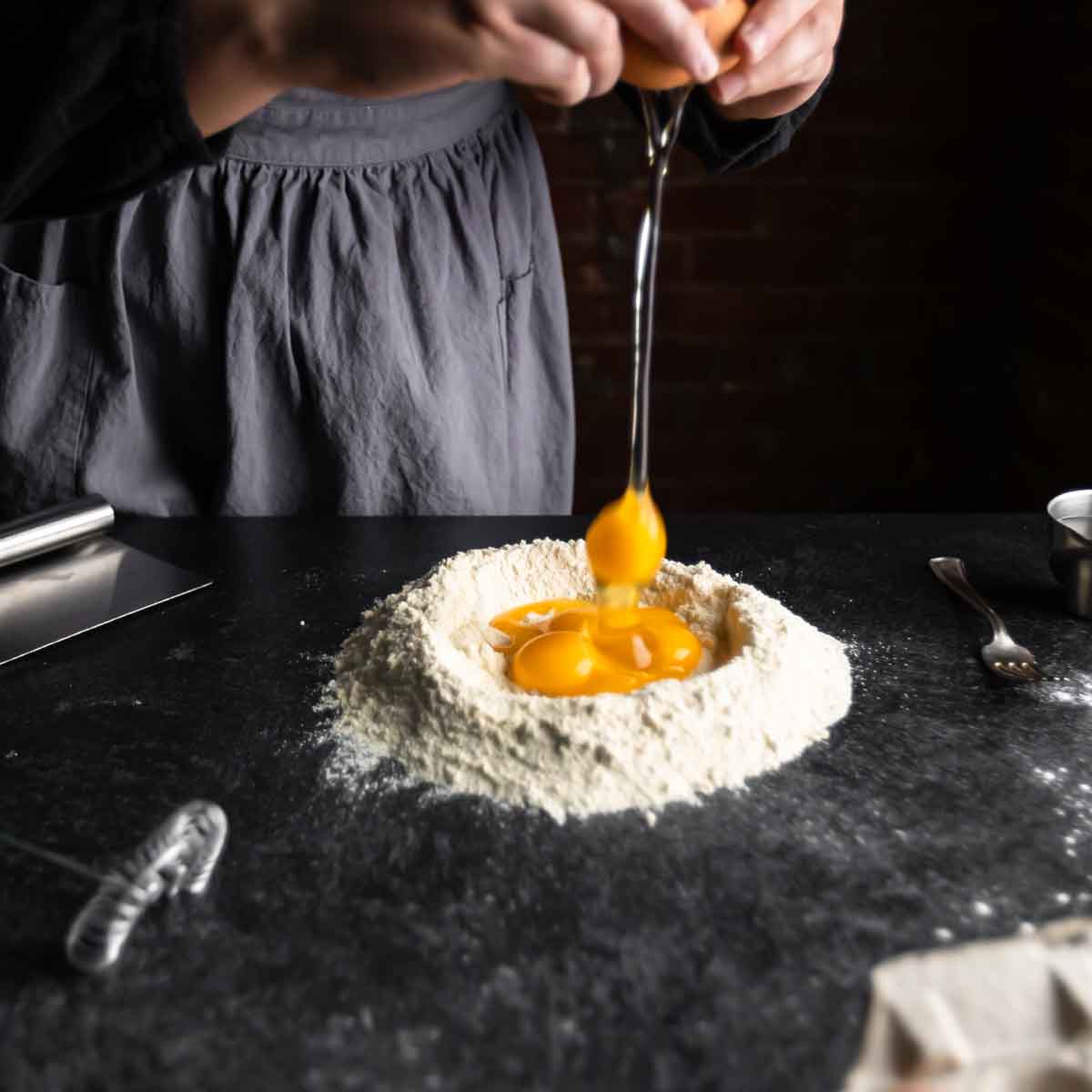 Cracking eggs into a well of flour on a black countertop.