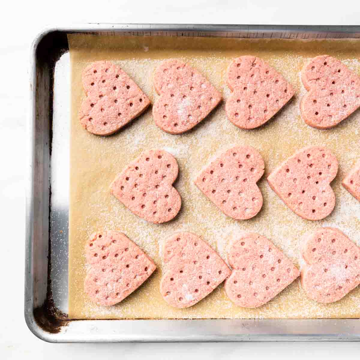 A sheet tray of perfectly baked strawberry heart cookies sprinkled with granulated sugar.