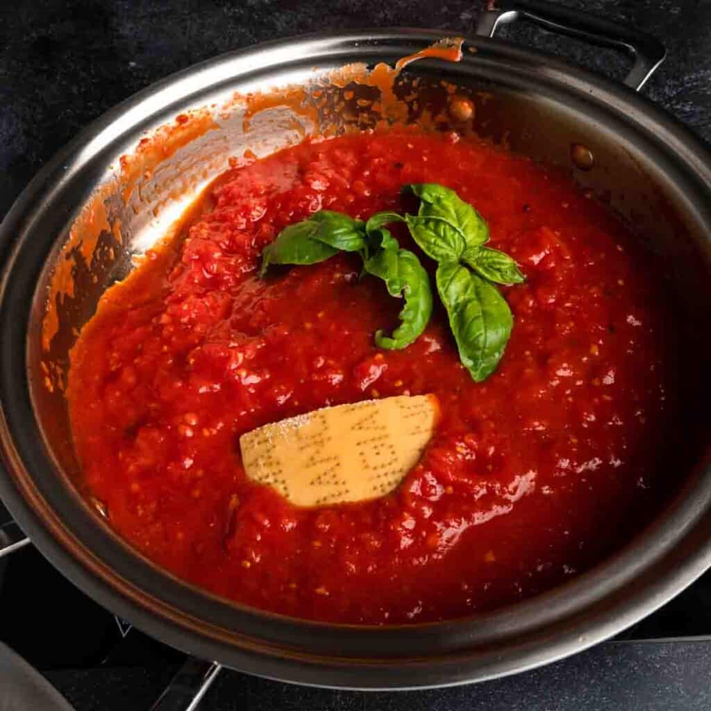 A Parmesan rind and fresh basil in a pan of homemade tomato sauce. 