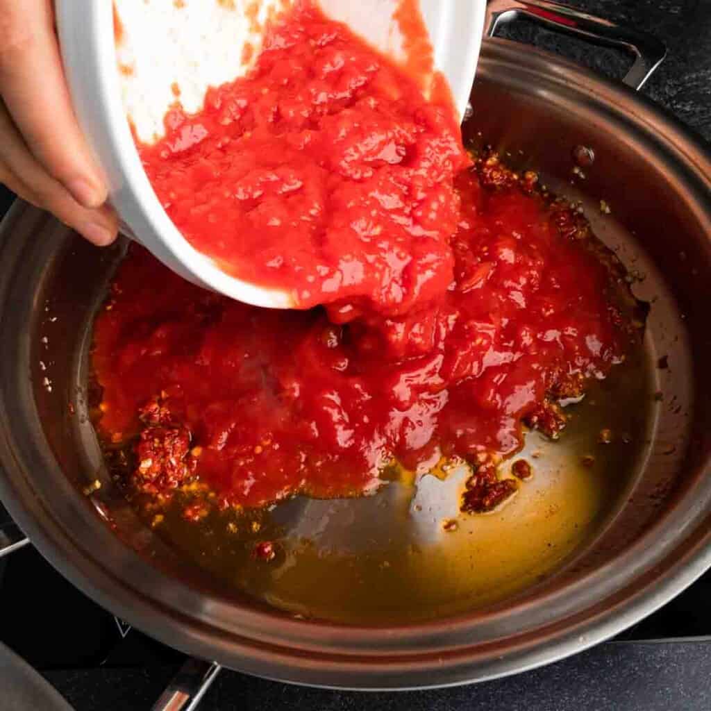 Adding crushed tomatoes to the sauce pan.