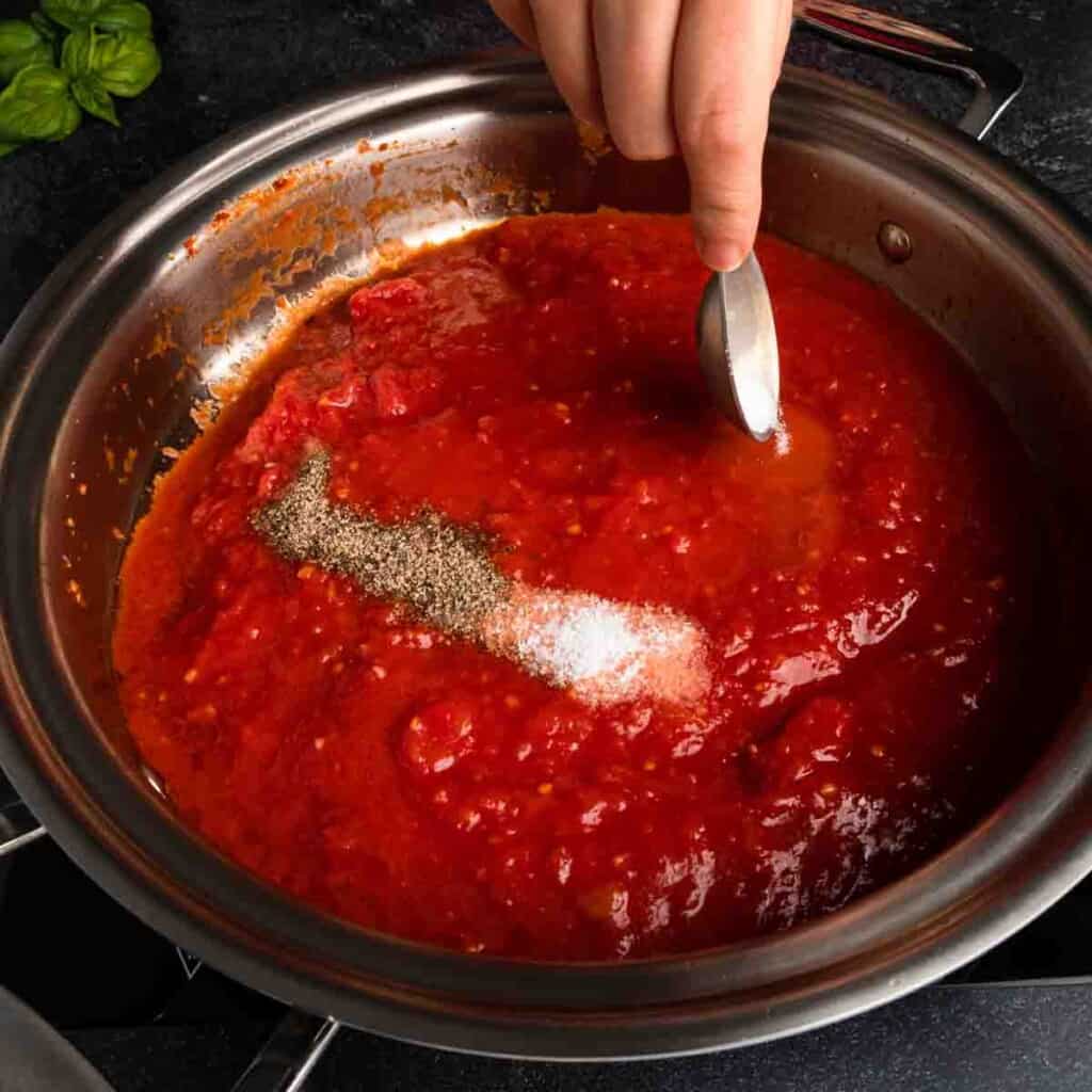 Adding salt, pepper and sugar into the San Marzano marinara sauce. 