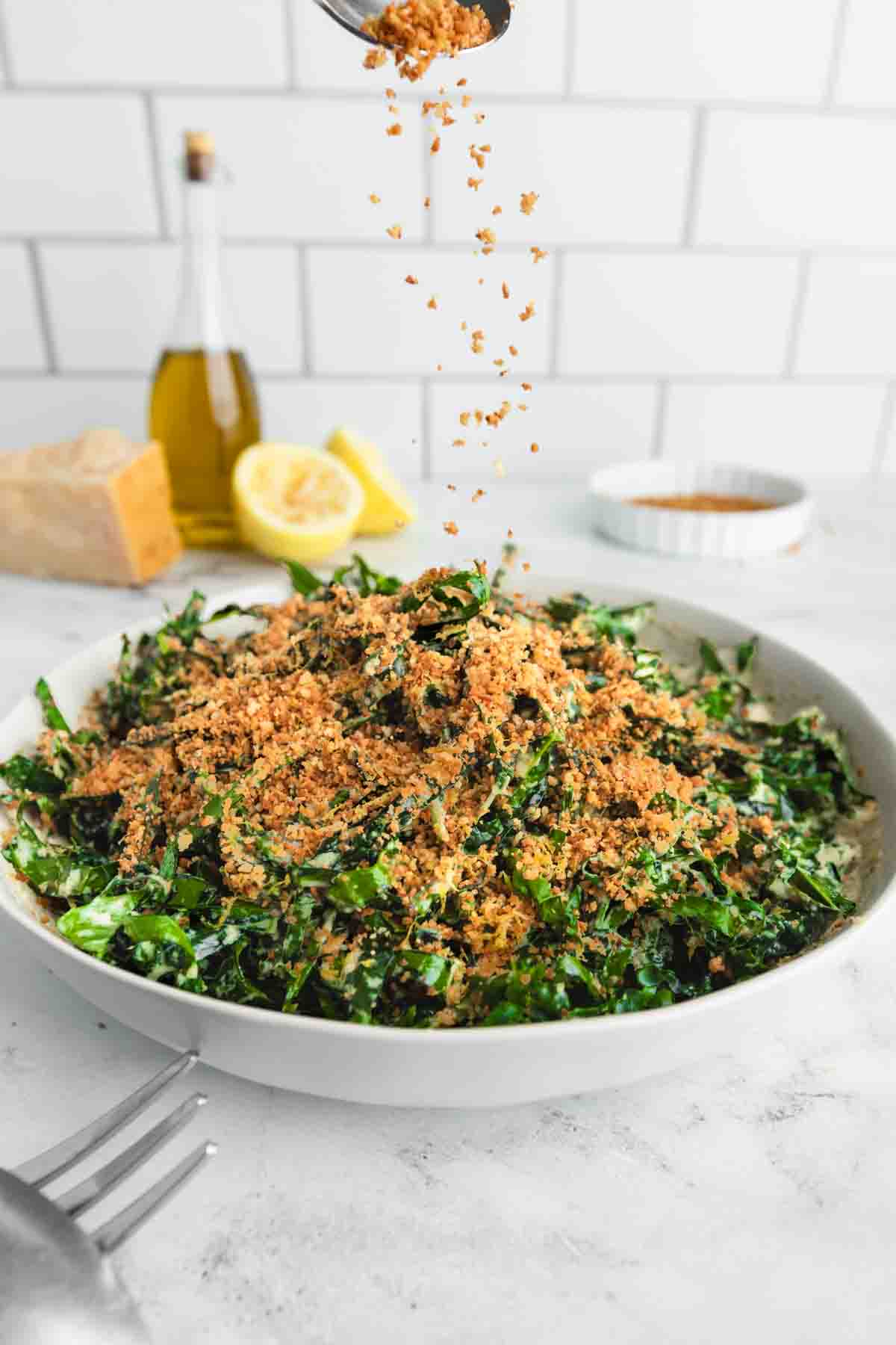 Sprinkling lots of lemon breadcrumbs over a serving bowl of Tuscan kale salad.