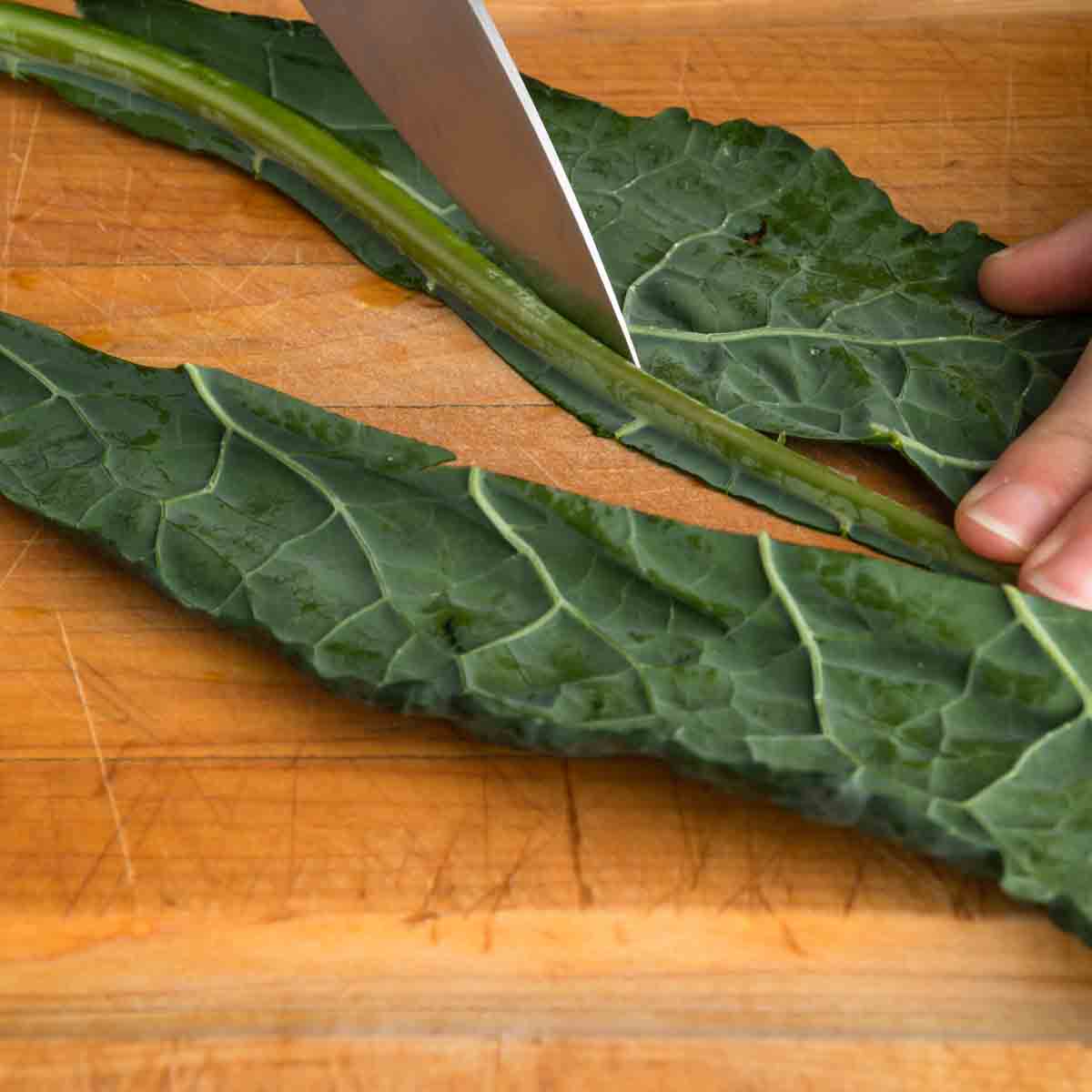 Using the tip of a knife to cut the rib out of a leaf of kale.